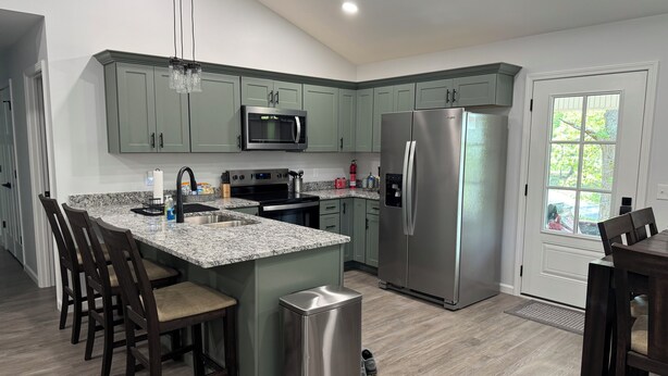 A modern kitchen with granite countertops, stainless steel appliances, and a large island with bar stools. - Kentucky Lake Retreat / 1 Mile to Jonathan Creek / Boat Parking (Benton)