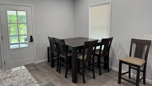 A dining area with a dark wooden table and chairs, a white door with a window, and a white wall with a window. - Kentucky Lake Retreat / 1 Mile to Jonathan Creek / Boat Parking (Benton)