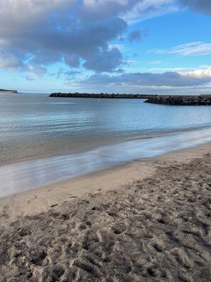 A beach with a rocky breakwater, calm water, and a clear sky. - Charming 1-bedroom apartment in delightful Praia da Vitória with AC, WiFi (Praia da Vitória)
