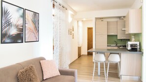 A modern kitchen with a bar area, a dining table with two chairs, and a sofa with cushions.