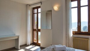 A bedroom with a bed, a desk, a window with a view, and a radiator.
