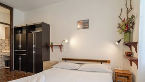 Hotelkamer met een bed, een houten nachtkastje, een klein tafeltje, een wandplank, een spiegel, een koelkast en een badkamer zichtbaar door een geopende deur.
