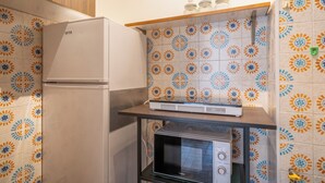 Een kleine keuken met een koelkast, magnetron en een plank met potten.