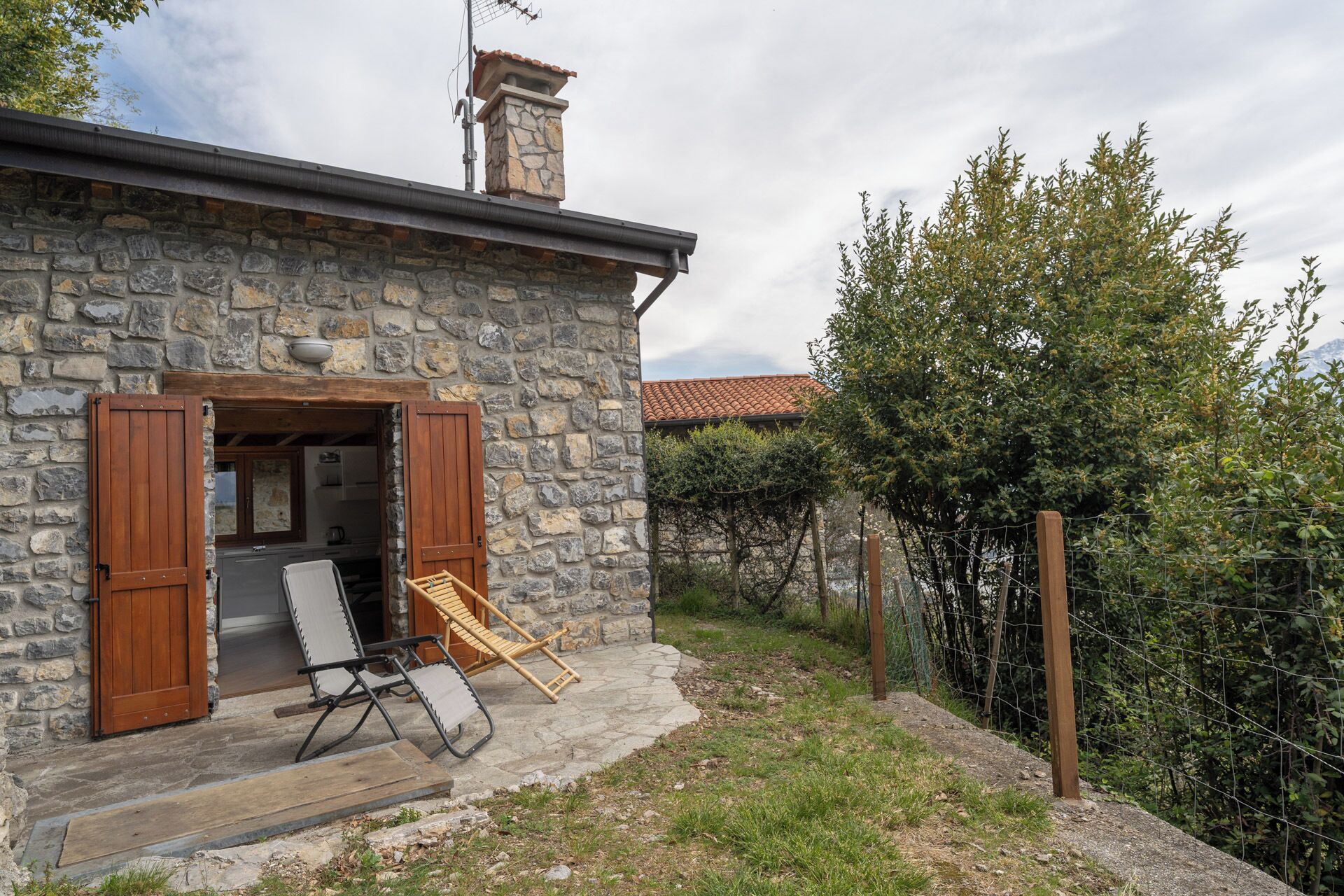 A stone house with a chimney, a wooden door, and a small porch with two chairs.
