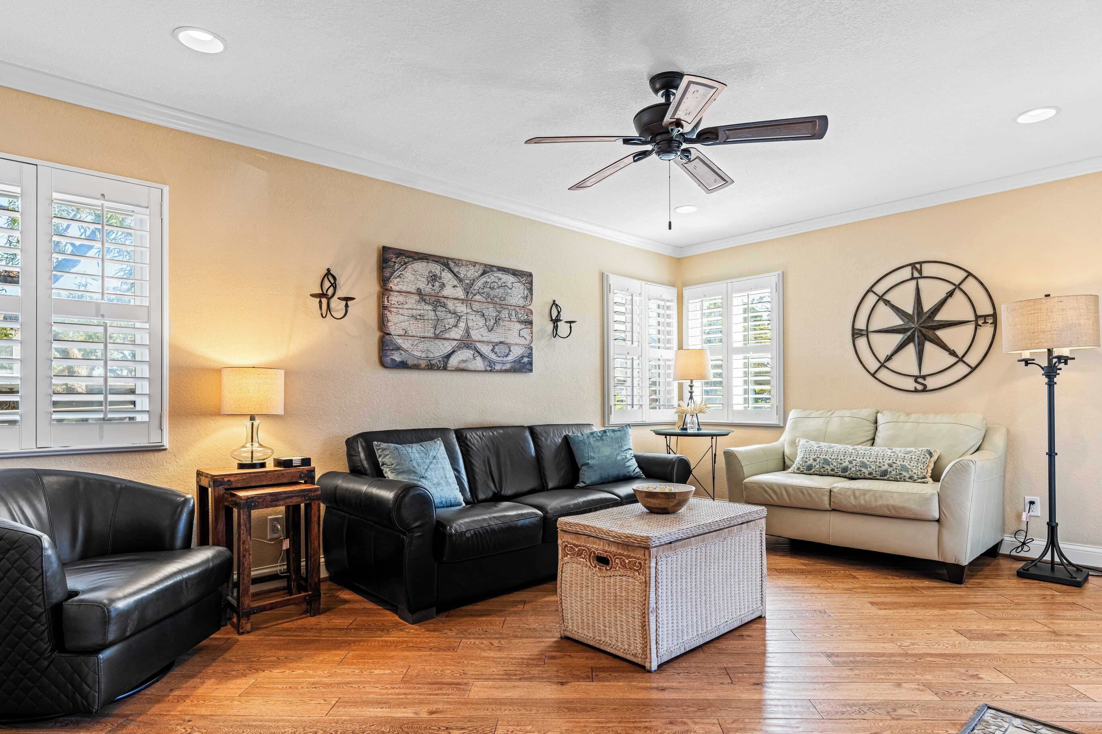 A living room with a black leather sofa, a beige sofa, a wooden coffee table, and a ceiling fan.