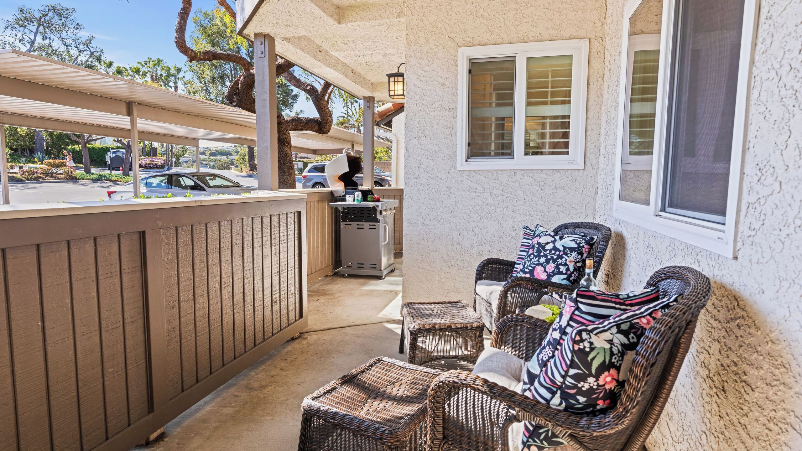 A covered outdoor seating area with wicker furniture, a wooden fence, and a view of the street.