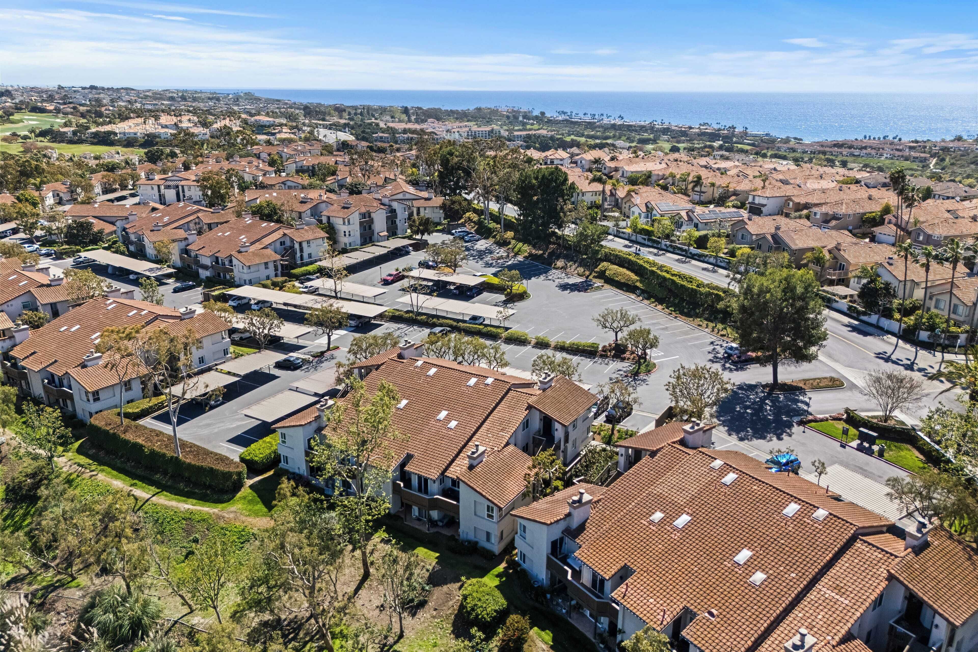 A residential area with multiple two-story houses, a parking lot, and a view of the ocean.