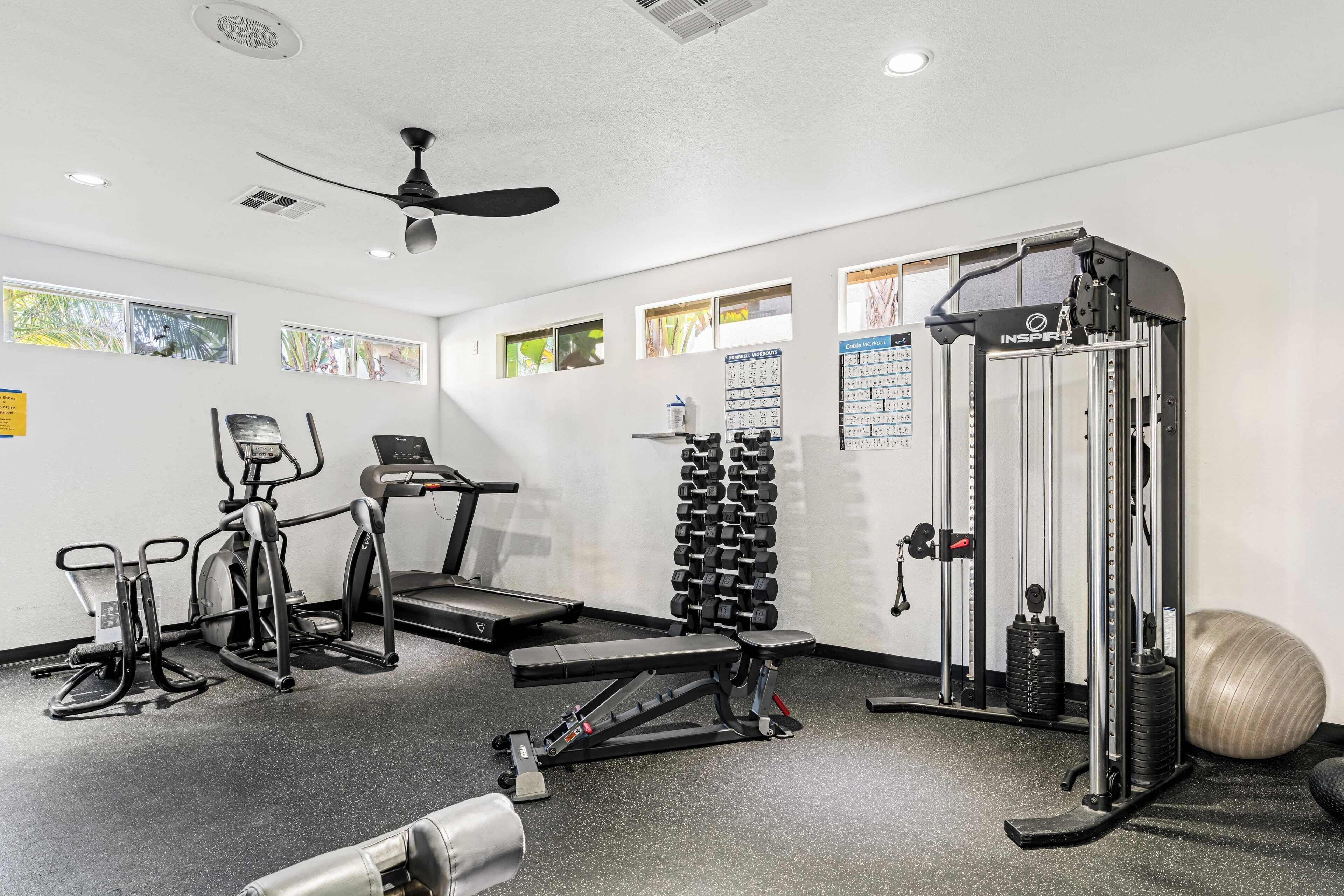 Une salle de sport équipée de machines de cardio, de poids libres et d’un support pour les exercices de squat.
