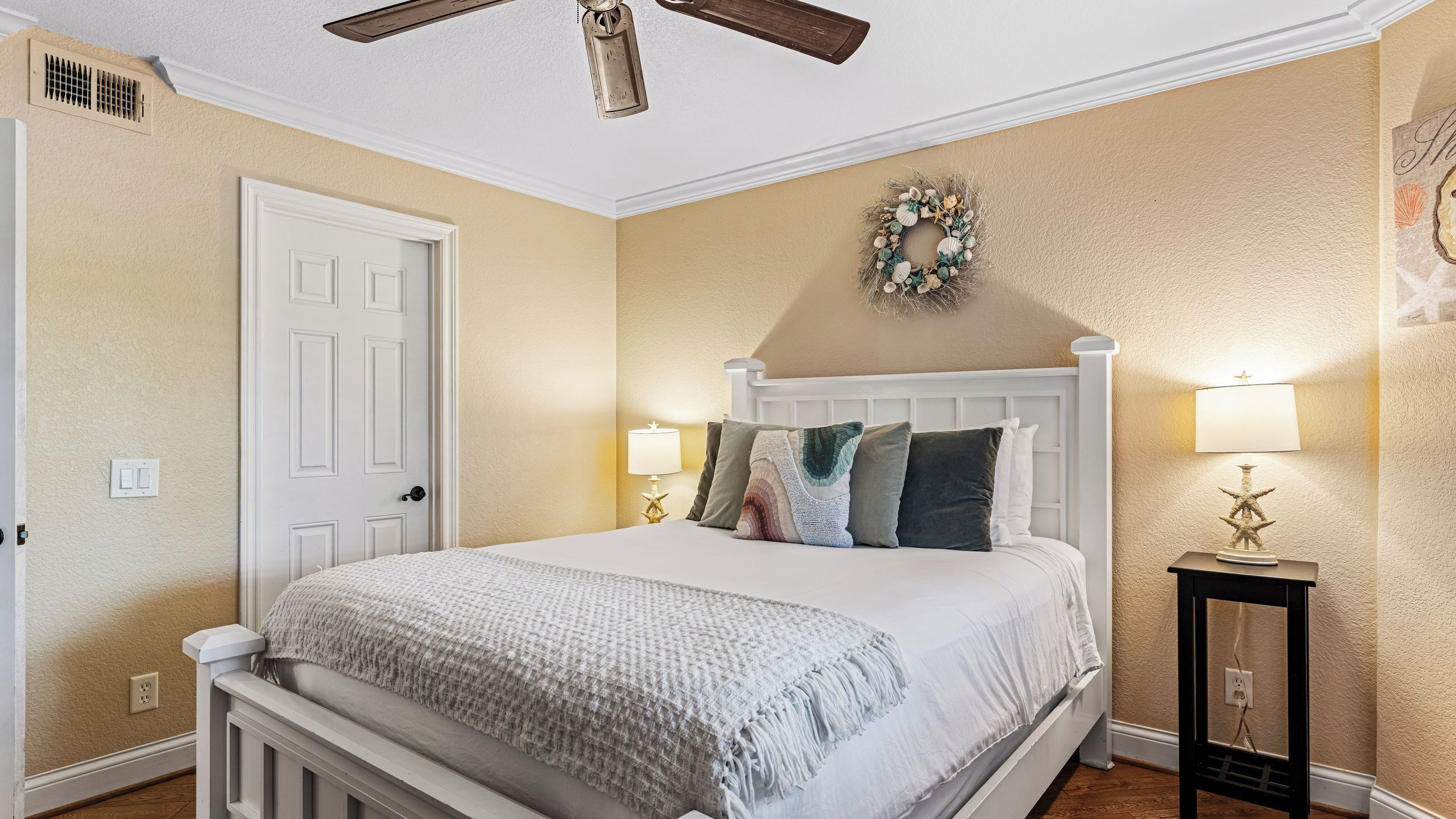 A bedroom with a bed, a ceiling fan, a wall-mounted lamp, and a decorative wreath.