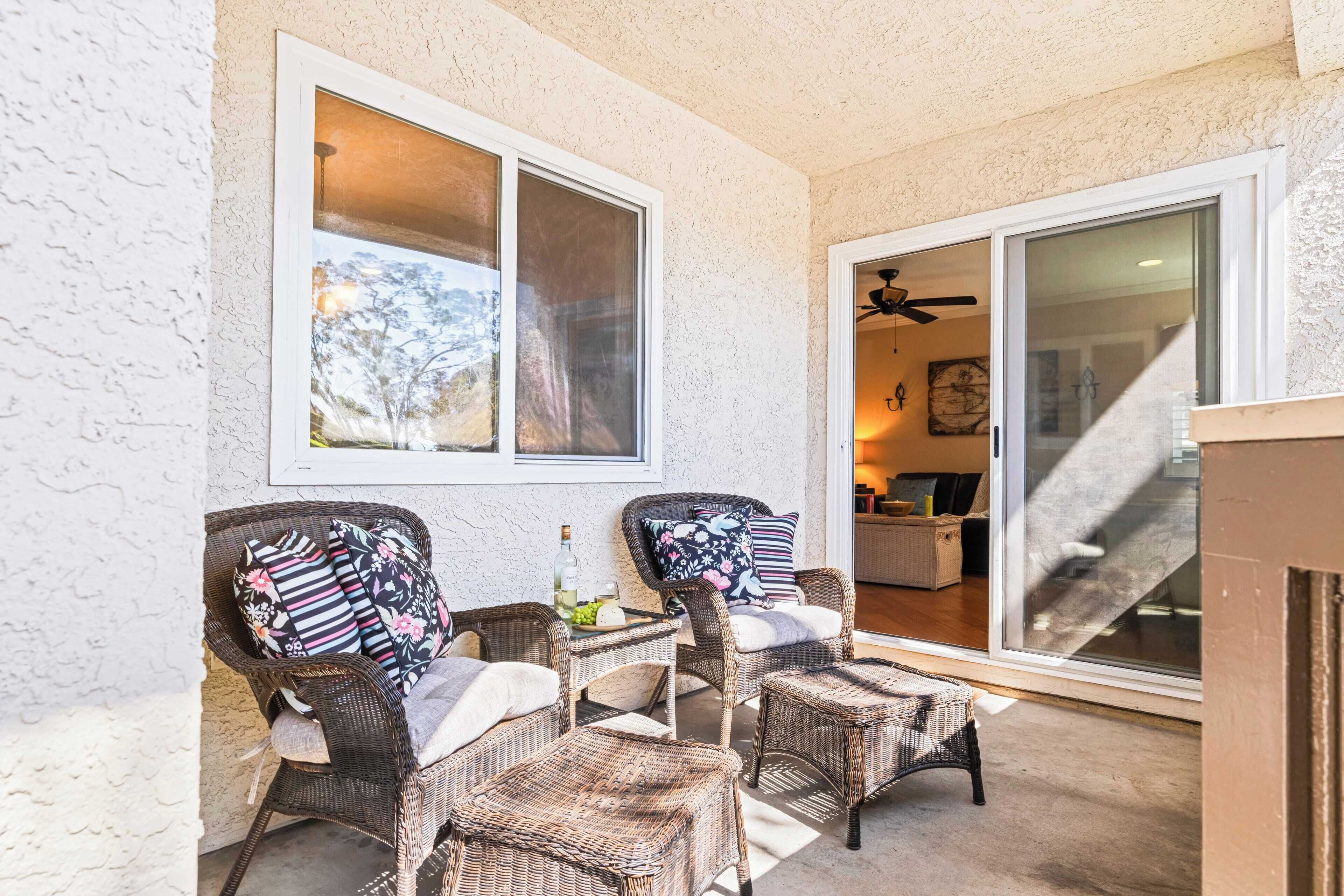 A covered patio area with wicker furniture, a glass door leading to an interior space, and a ceiling fan.