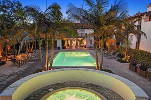 A pool area with lounge chairs and a hot tub, surrounded by palm trees and a building with a balcony.