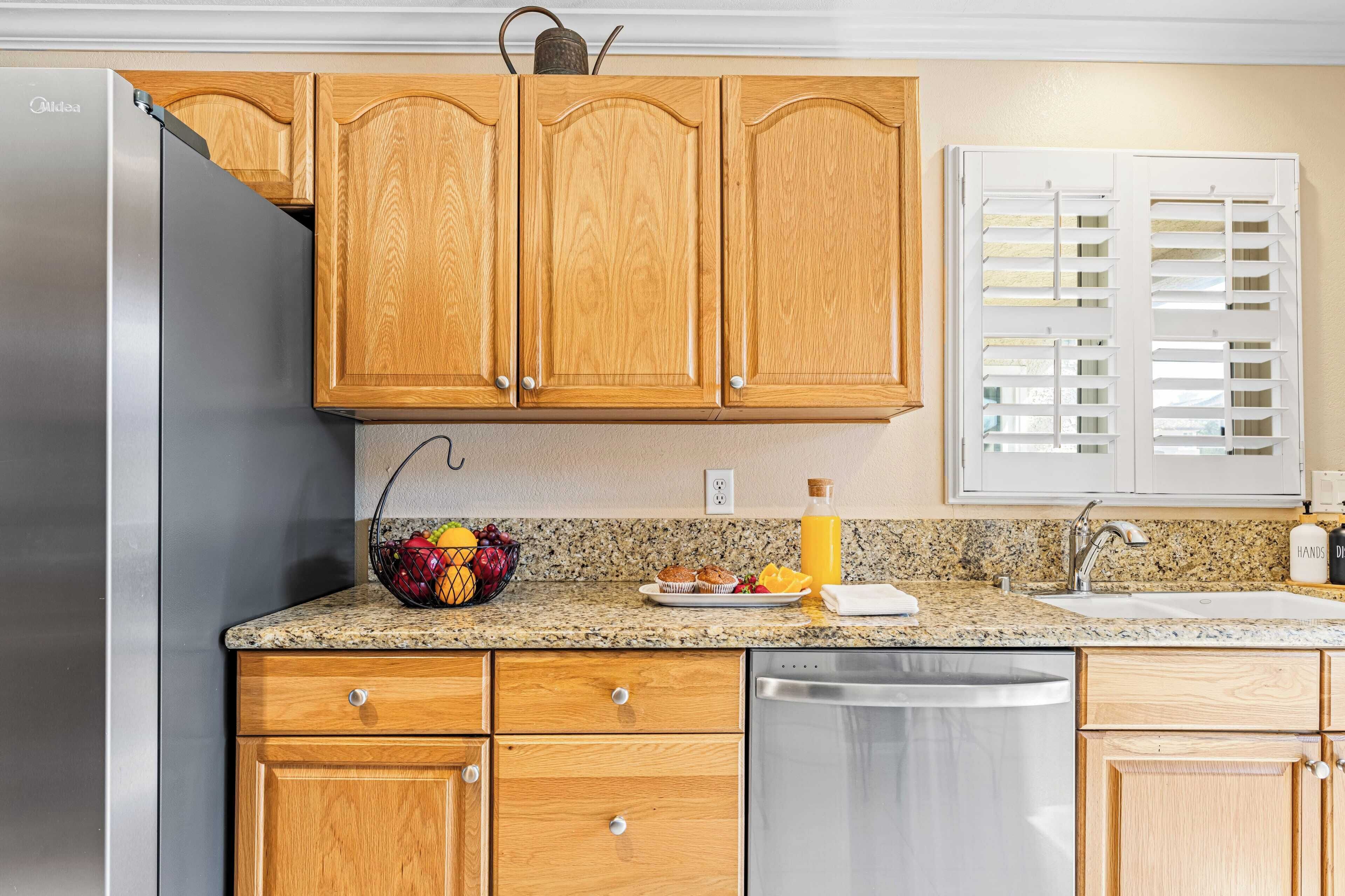 A kitchen with wooden cabinets, a stainless steel refrigerator, a granite countertop, a sink, and a dish rack.