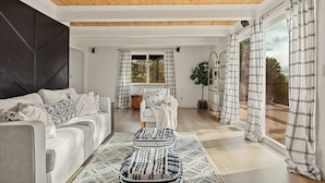 Un salon moderne avec un canapé, un pouf et une grande fenêtre agrémentée de rideaux.