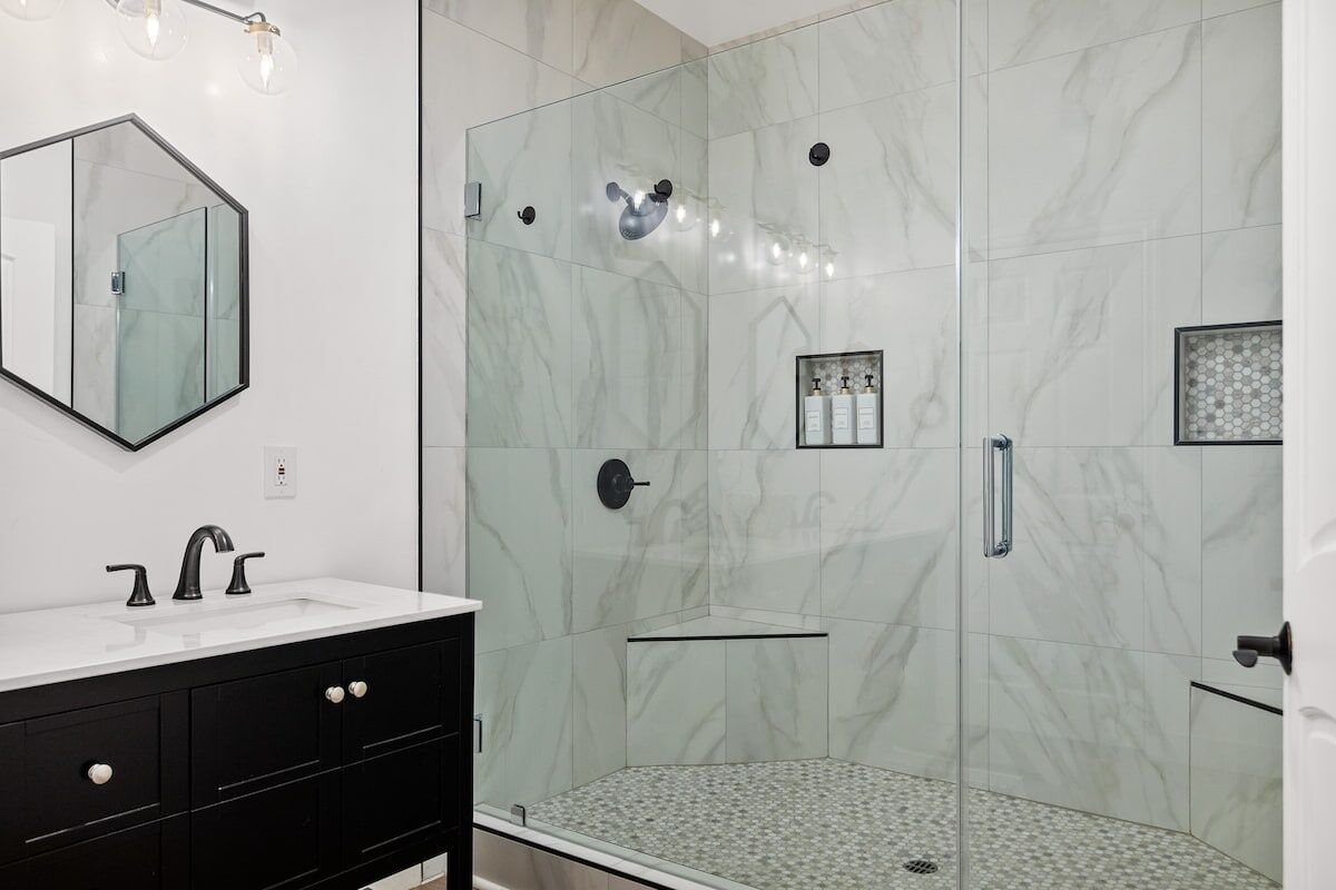 Un baño moderno con ducha de vidrio, un lavamanos blanco y muebles negros, y un espejo grande.