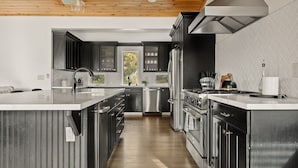 Une cuisine moderne avec des meubles de couleur sombre, des appareils électroménagers en acier inoxydable et un plafond en bois.