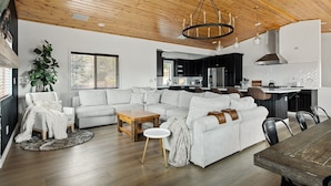 Un salon moderne avec un plafond en bois, un grand canapé, une table basse et une table à manger.