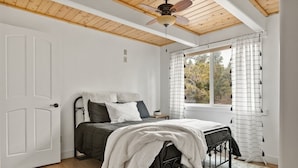 Une chambre à coucher avec un lit, un ventilateur de plafond, une fenêtre avec des rideaux et une porte.
