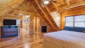 A wooden cabin bedroom with a bed, dresser, and a TV.