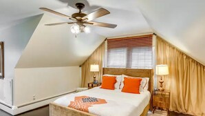 Une chambre avec un plafond en pente, un lit avec des coussins orange, deux lampes de chevet et un ventilateur de plafond.