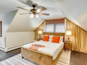 A bedroom with a sloped ceiling, a bed with orange pillows, two bedside lamps, and a ceiling fan. - 4BR/2BA Home with Private Pool – 5 Min to Bucknell University – Sleeps 12 (Lewisburg)