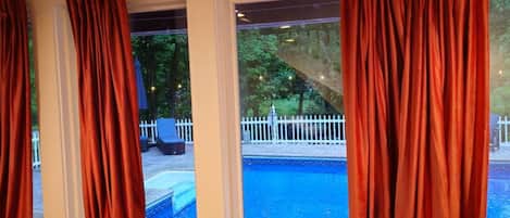 Habitación con vista a una piscina, cortinas rojas y una valla blanca.