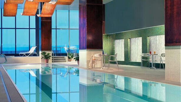 An indoor swimming pool with lounge chairs and tables, large windows, and a view of the sky. - The Tower at Turning Stone Resort Casino (Verona)
