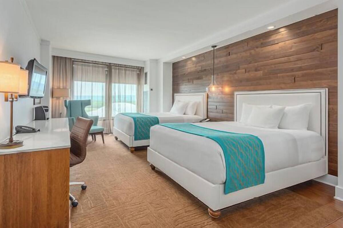 A hotel room with two beds, a desk, a chair, and a TV.
