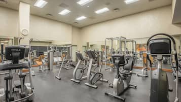 Un gimnasio con diferentes máquinas de ejercicio, espejos y un reloj en la pared.