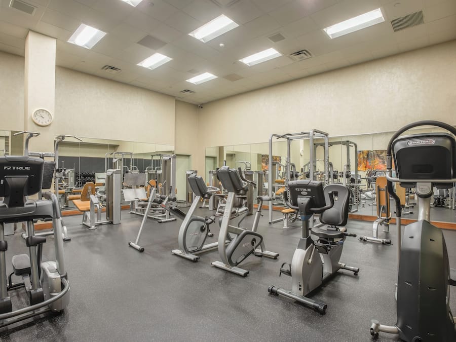 A gym with various exercise machines, mirrors, and a clock on the wall.