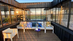 Un espace extérieur moderne, aménagé avec des sièges, protégé par une paroi de verre, doté de mobilier blanc et offrant une vue sur le paysage.