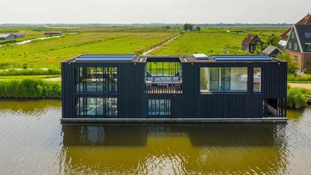 Une péniche moderne dotée d’un toit plat, de grandes fenêtres et d’une terrasse.