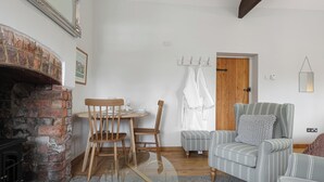 Un salon chaleureux avec une cheminée, une table à manger avec des chaises, un fauteuil à rayures et une porte en bois.