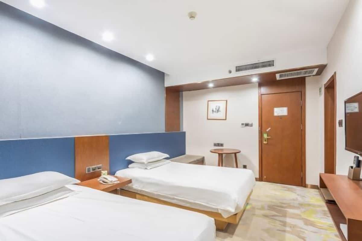 A hotel room with two beds, a small table, a chair, a desk, a TV, and a door.