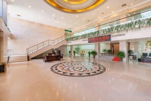 A spacious lobby with a central circular design, a staircase, and a second-floor balcony with plants. - Zhoukou Hotel (Zhoukou Wanshunda Department Store) (Zhoukou)