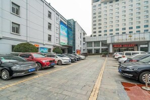 A parking lot with multiple cars, a hotel building with signage, and a tall building in the background. - Zhoukou Hotel (Zhoukou Wanshunda Department Store) (Zhoukou)