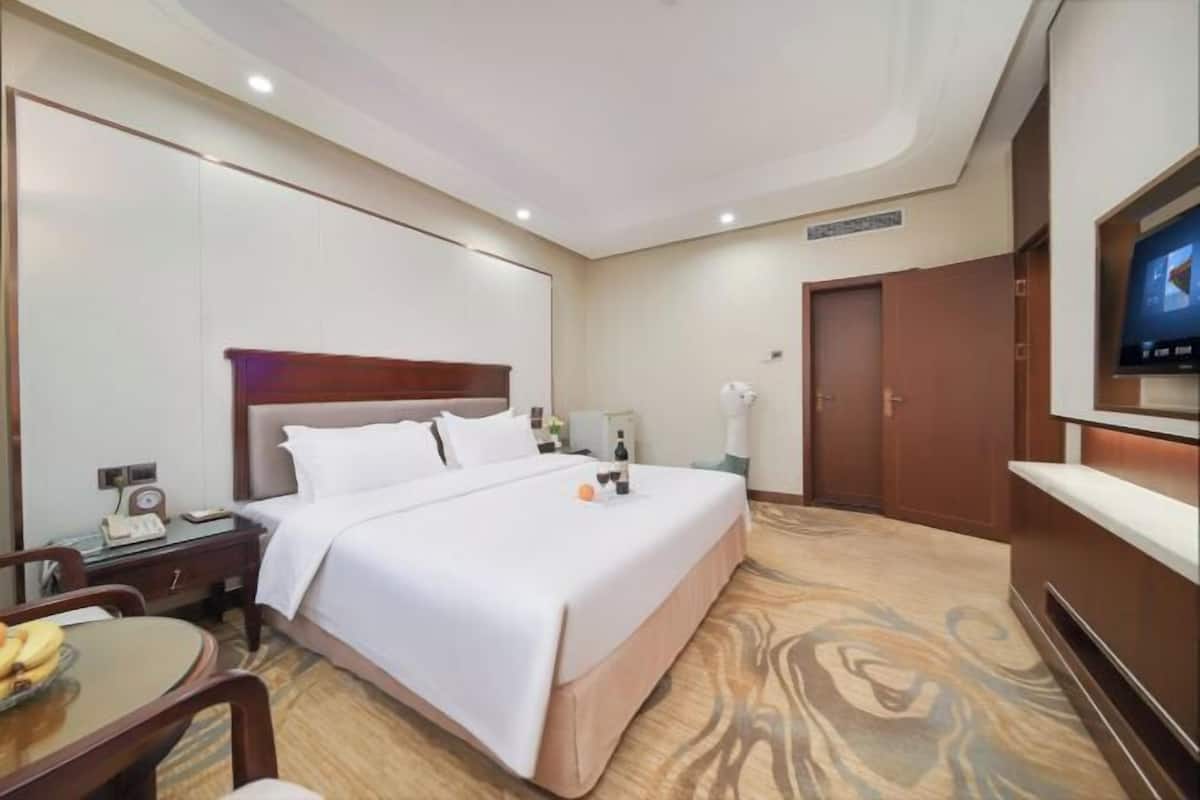 A hotel room with a large bed, a desk with a telephone, a television, and a small table with a fruit bowl.