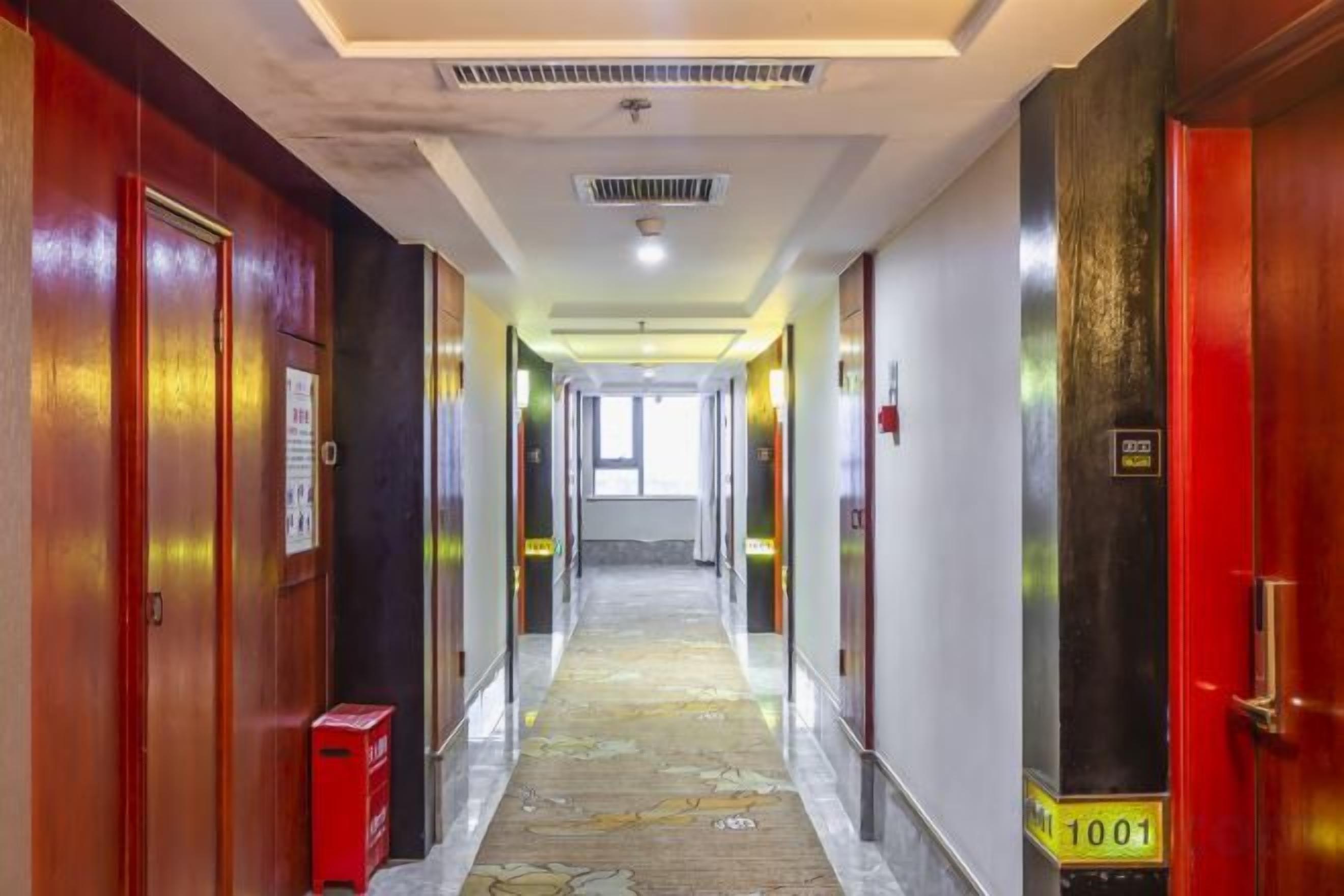 Un pasillo de hotel con puertas a ambos lados, un detector de incendios a la derecha y un extintor a la izquierda.