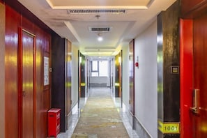 A hotel hallway with doors on both sides, a fire alarm on the right, and a fire extinguisher on the left. - Zhoukou Hotel (Zhoukou Wanshunda Department Store) (Zhoukou)