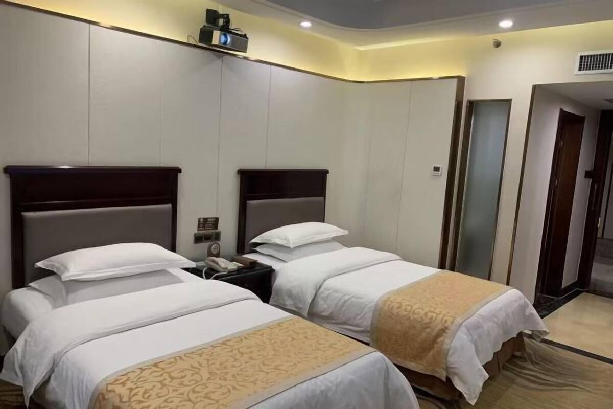A hotel room with two beds, a nightstand with a phone, and a wall-mounted TV.