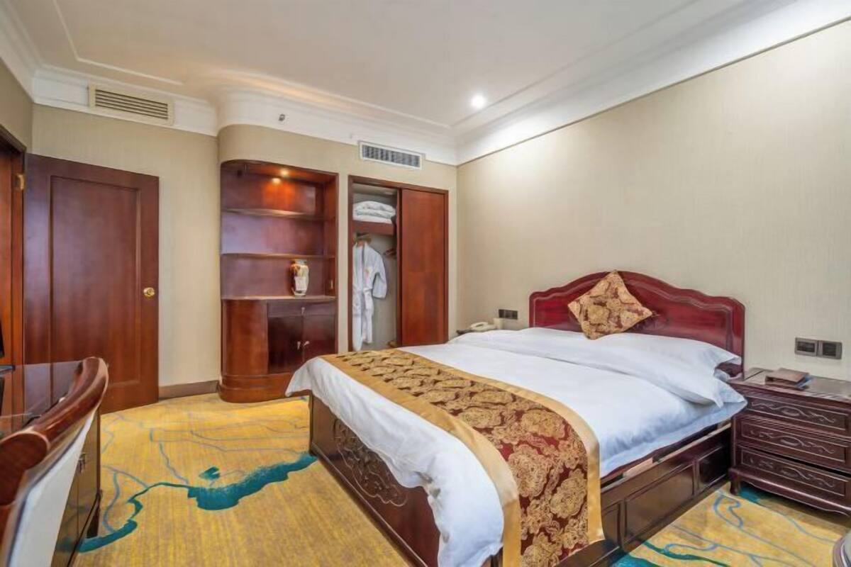 A hotel room with a bed, a wardrobe, a desk, and a chair.