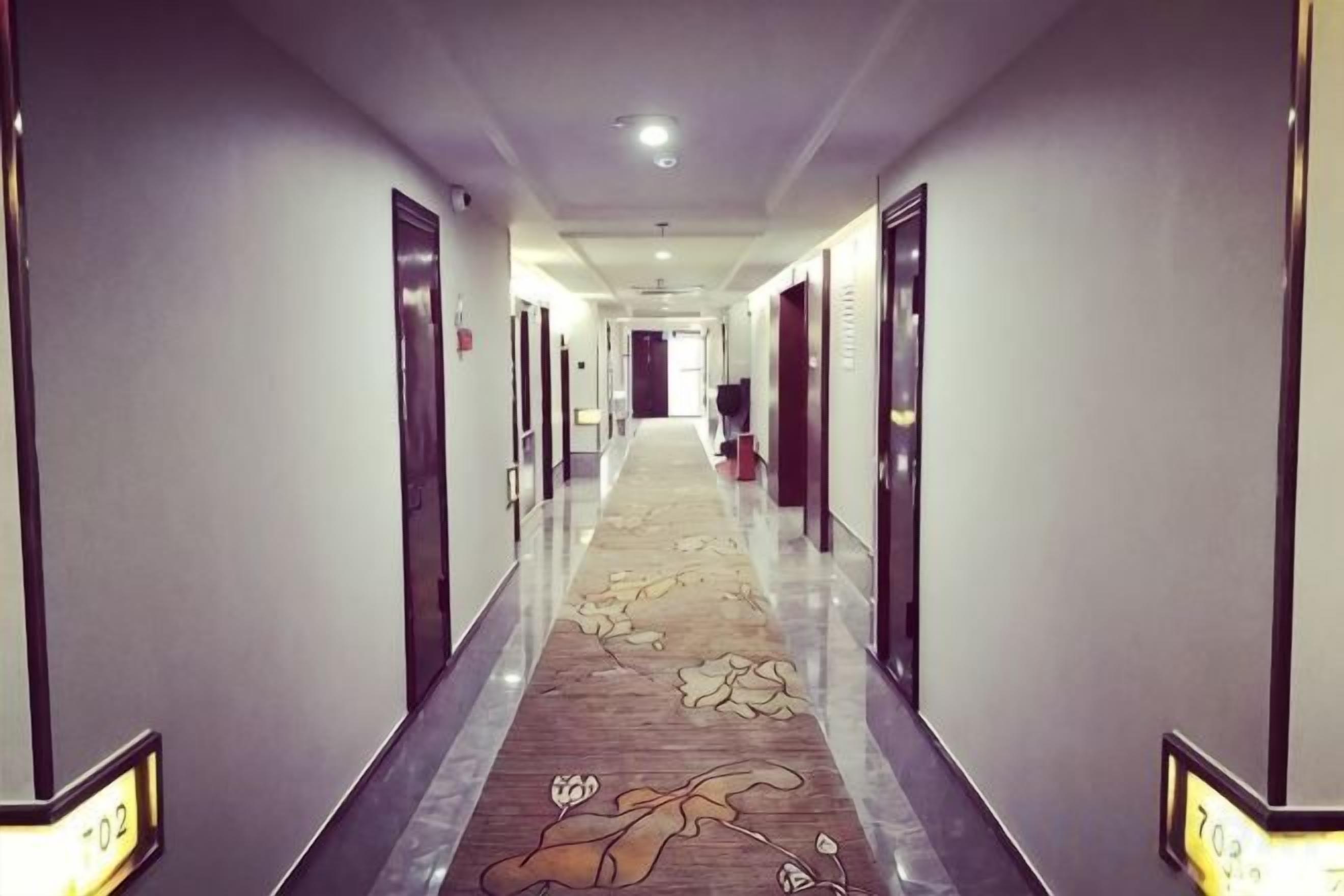 A hotel hallway with doors on both sides, a carpeted floor, and a number sign on the wall.