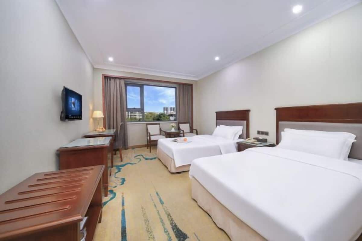 A hotel room with two beds, a desk, a chair, and a TV.