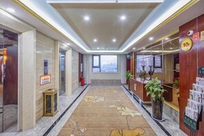 A hotel lobby with a reception desk, a plant, a carpet with leaf patterns, and a city view through the windows. - Zhoukou Hotel (Zhoukou Wanshunda Department Store) (Zhoukou)
