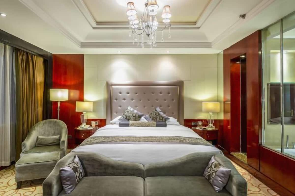 A hotel room with a large bed, two bedside tables, a chandelier, a chair, and a large mirror.