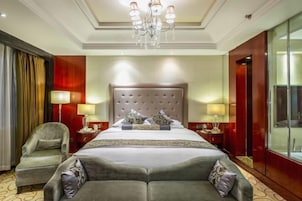 A hotel room with a large bed, two bedside tables, a chandelier, a chair, and a large mirror.