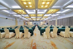Un salón de conferencias con mesas y sillas dispuestas en filas, una alfombra estampada e iluminación empotrada en el techo.