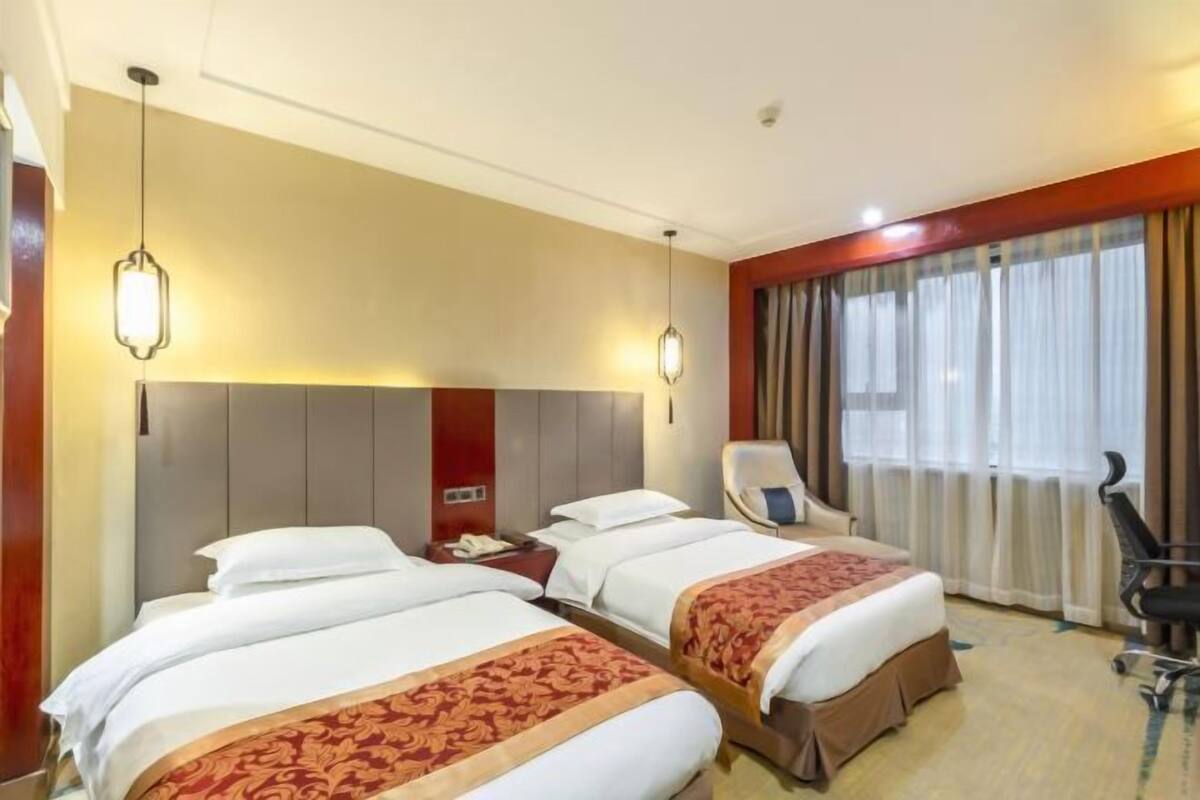 A hotel room with two beds, a desk, a chair, and a large window with curtains.