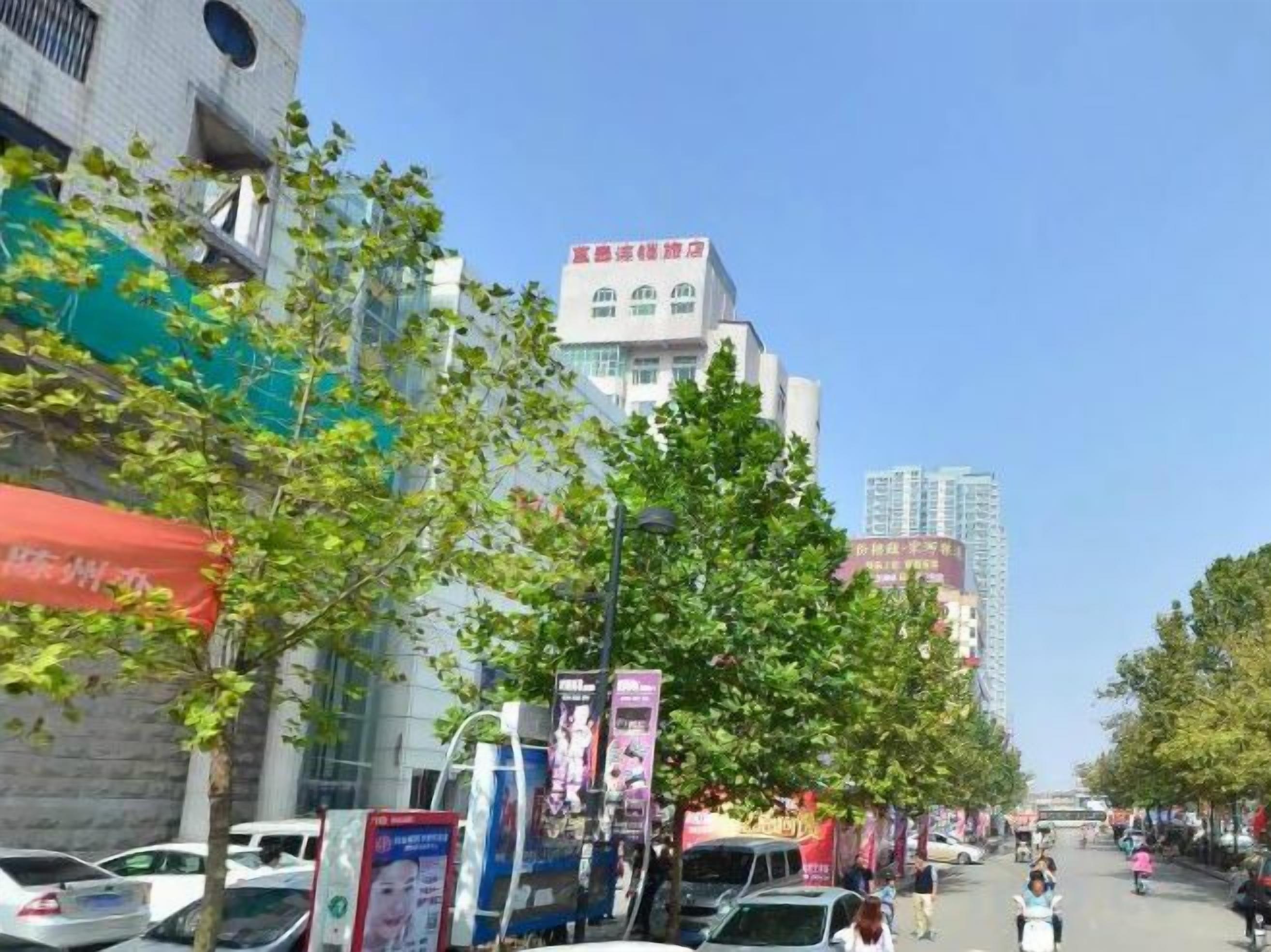 Una calle con coches estacionados, árboles y edificios con rótulos.