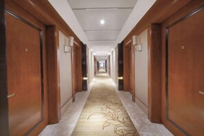 Un pasillo de hotel con puertas de madera, alfombra estampada y una lámpara en el techo.