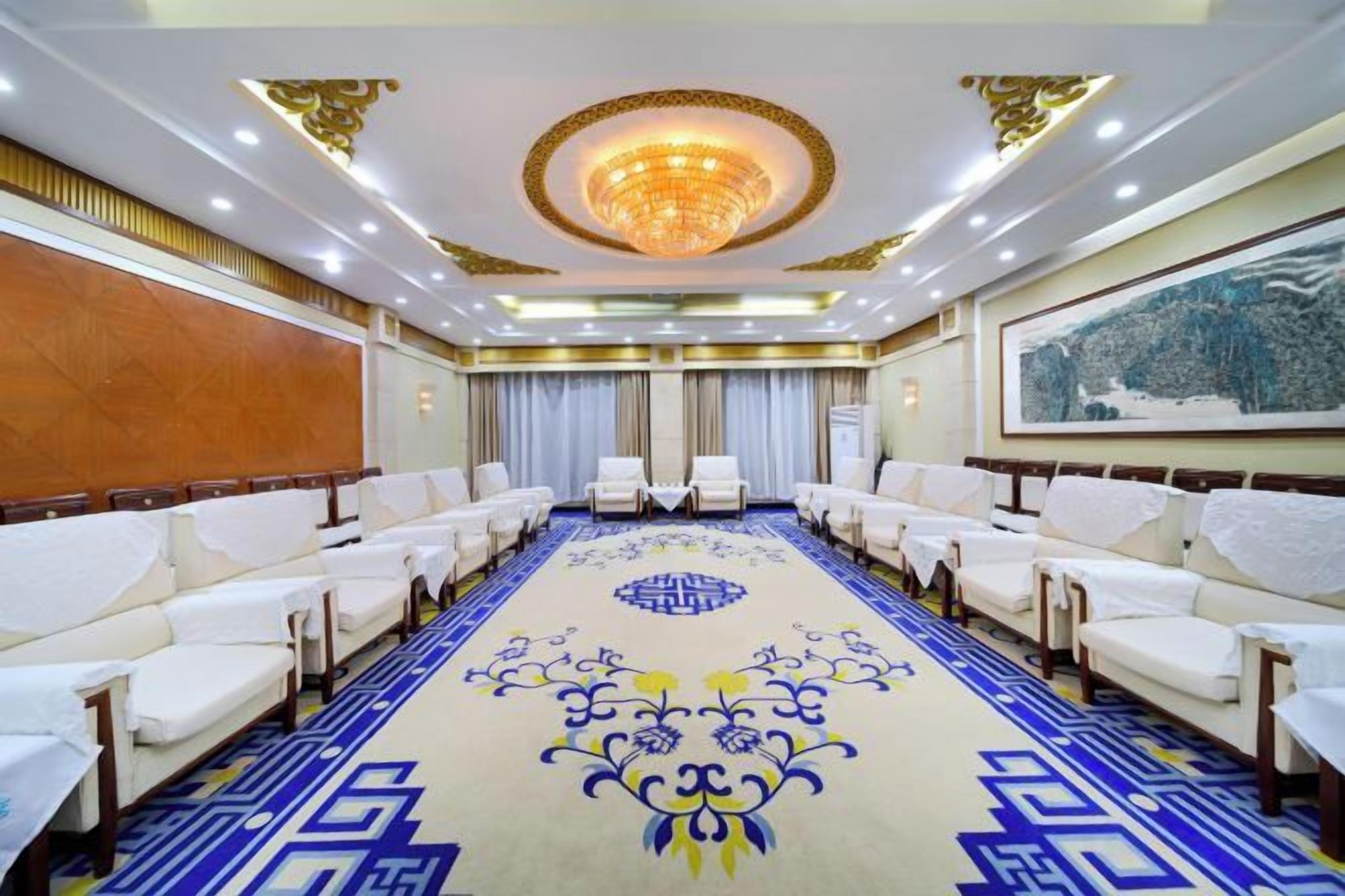 Un salón de conferencias con una larga mesa, sillas blancas y una alfombra estampada.